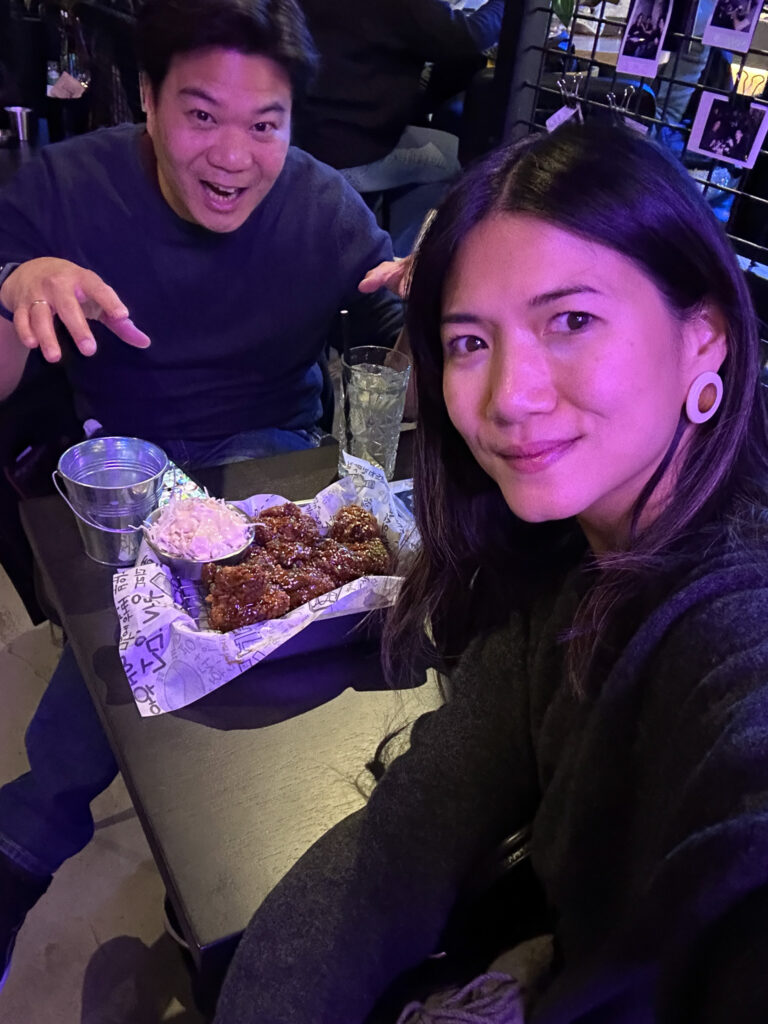 A selfie of us at the korean street food restaurant with a plate of fried chicken on the table.